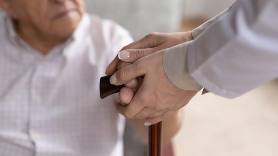 Mujer envuelve las manos de un anciano que sostiene un cayado con las suyas